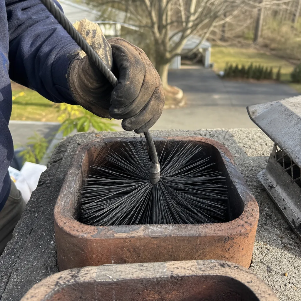 Professional chimney sweep using a wire brush to clean a chimney flue
